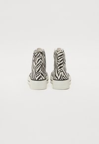 Høye sneakers med et zebra-stripe mønster i svart og hvitt, med hvite gummisul og teksturerte sider.
