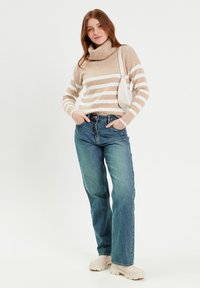 Suéter a rayas beige y blanco con cuello alto, combinado con jeans rectos azul y zapatos de plataforma color crema. Incluye un bolso de hombro blanco.