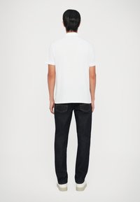 Hvid polo t-shirt med et simpelt design, parret med mørkeblå jeans og hvide sneakers. Poloen har korte ærmer og en krave.