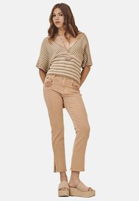 Jersey beige de punto con escote en V, combinado con unos jeans ajustados de color beige claro con detalles bordados y aberturas en los tobillos. Sandalias de plataforma beige.