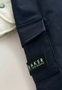 Marineblaue Jackenärmel mit einer Tasche; weist ein schwarzes Etikett mit der weißen Aufschrift "BAKER by TED BAKER" auf. Der Stoff wirkt glatt und strapazierfähig.