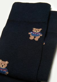 Marineblau Socken aus einem Baumwollgemisch mit einer weichen Textur. Mit einem gestrickten Bärendesign auf der Seite, der einen blauen und roten Pullover trägt.