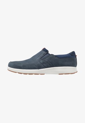 Donkerblauwe slip-on casual schoen met witte zool, geperforeerd zijdetail en slipvaste rubberen buitenzool.