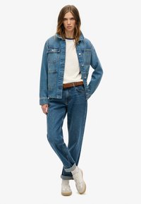 Lyseblå denimjakke med to frontlommer, parret med matchende blå jeans. Under jakken en cremet skjorte stoppet ned i bukserne, brun bæltetaske og beige sneakers.