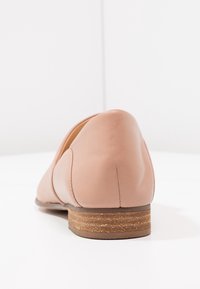 Chaussure en cuir rose avec une forme arrondie, un petit talon empilé et des accents cousus. Texture lisse et design minimaliste.