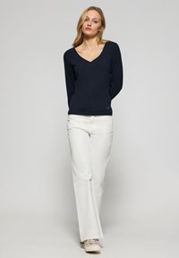 Top a maniche lunghe blu navy con scollo a V abbinato a pantaloni bianchi dritti, caratterizzati da una texture liscia e un logo discreto vicino all'orlo.