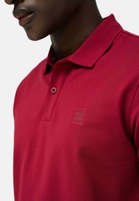 Polo rosso con tessuto testurizzato, dotato di un colletto con due bottoni e di un piccolo logo in rilievo "Salsa Jeans" sul petto.