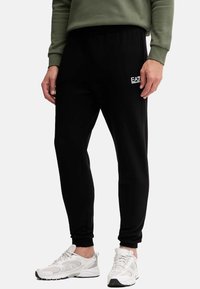 Pantaloni sportivi neri in tessuto morbido, con vita elastica, vestibilità affusolata e piccolo logo bianco sul lato.