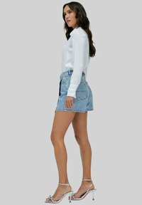 Shorts de denim en azul claro, de talle alto con dobladillo deshilachado, combinados con una camisa blanca de manga larga y tacones de tira plateados.