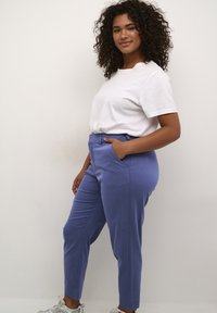 Pantaloni su misura azzurri chiari con una texture liscia, tasche frontali e gamba leggermente affusolata. Abbinati a una t-shirt in cotone bianca.