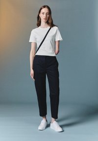 Hvit t-skjorte med korte ermer, marineblå bukser og hvite joggesko. Svart skulderreim over kroppen. Glatt stoff, avslappet passform, minimal design.