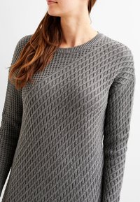 Grauer Strickpullover mit einem strukturierten Rautenmuster, rundem Ausschnitt und langen Ärmeln. Er zeichnet sich durch ein figurnahes Design und ein weiches Material aus.
