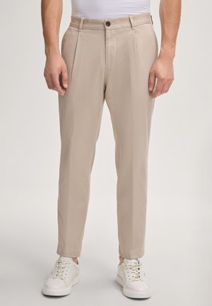 Beige, tapered Hosen mit vorderen Falten, aus leichtem Stoff, kombiniert mit weißen Sneakers. Einreihiger Knopfverschluss.
