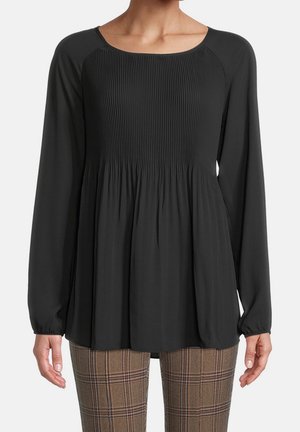 Zwarte blouse met lange mouwen en geplooide voorkant, gedragen met bruine geruite broek, zichtbaar van schouders tot heupen, handen ontspannen langs het lichaam.