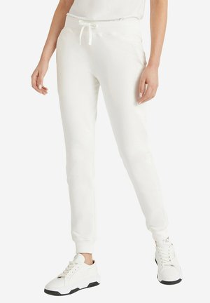 Pantalons de survêtement blancs, ajustés, avec une texture douce, une taille élastique et un cordon de serrage ajustable, associés à des baskets blanches avec des accents noirs.