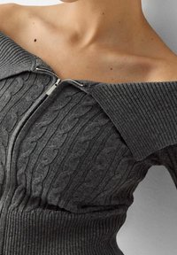 Gray knitted sweater featuring a cable knit pattern, off-the-shoulder design, and a front zipper with a ribbed collar and hem.