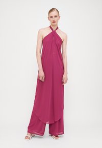 Robe sans manches à col halter en fuchsia, fabriquée en tissu léger ; elle présente un large pantalon fluide et une ouverture en forme de trou de clé à l'avant.