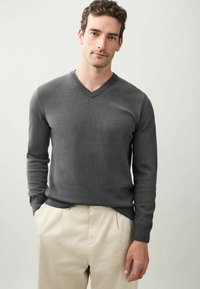 Dunkelgrauer Strickpullover mit V-Ausschnitt, langen Ärmeln und gerippten Bündchen, kombiniert mit hellbeigen Hosen für einen Kontrast.