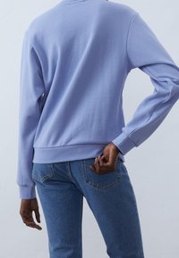 Felpa viola con maniche lunghe, texture morbida, polsini e fascia in costina, abbinata a jeans di denim blu con tasche sul retro.