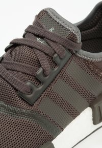 Dark brown athletic shoe featuring mesh material, gray accents, textured sides, and a white sole, with laces and distinctive stripe design.