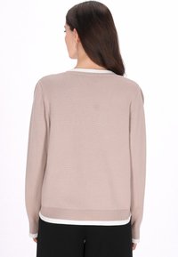 Világos tengeri csiga színű pulóver sima textúrával, bordázott mandzsettákkal, valamint fehér szegéllyel a nyakkivágásnál és az alján. Laza szabású és hosszú ujjú.