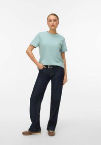 Lichtblauw T-shirt met korte mouwen en een ronde hals, gecombineerd met donkerblauwe jeans met wijde pijpen en bruine schoenen. Eenvoudig, onopvallend ontwerp.