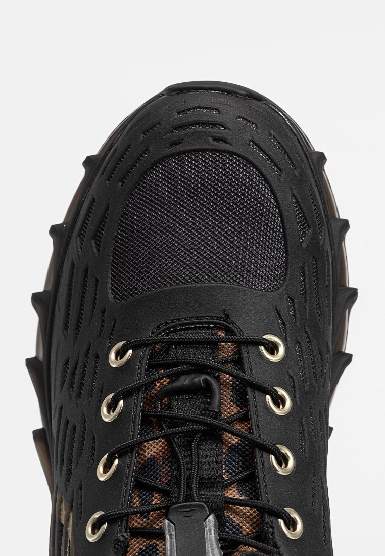 Schwarzer Sportschuh mit strukturiertem Obermaterial, Netzdetails und ausgeprägtem Schnürsystem. Besitzt goldene Ösen und eine robuste, konturierte Sohle.