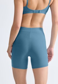 Blå sportshorts gjorda av slätt, elastiskt tyg med hög midja. Bakifrån syns diskreta sömmar och en figurnära design.