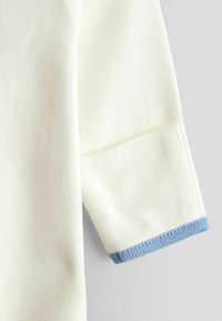 Langærmet hvidt stof med et nærbillede af en ærmekant med lyseblåt ribbet bånd.