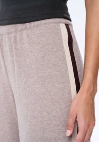 Lichtbruine joggers gemaakt van zacht materiaal, met een geribde tailleband en contrasterende verticale strepen in crème en bordeauxrood.