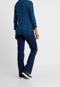 Blå mönstrad topp med trekvartsärmar, kombinerad med mörkblå jeans. Skorna är svarta sneakers med vita sulor och detaljer.