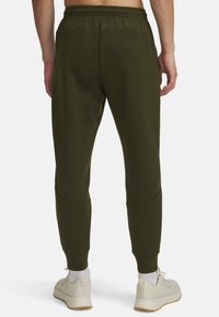 Olive green jogger pants made of soft fabric, featuring an elastic waistband, tapered legs, and ribbed cuffs, paired with beige sneakers.