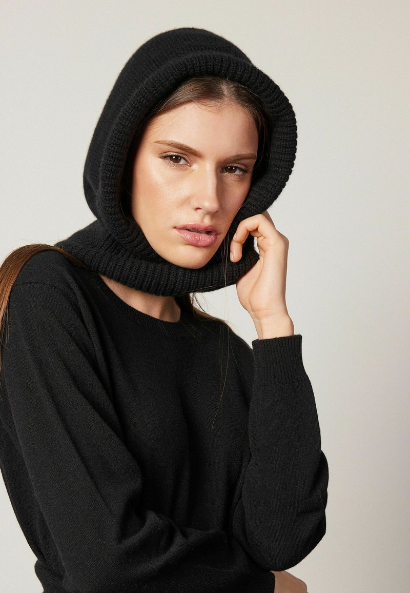 Svart stickad huva med en texturerad yta, designad för att passa tätt runt halsen och huvudet. Slät tyg med ribbade kanter.