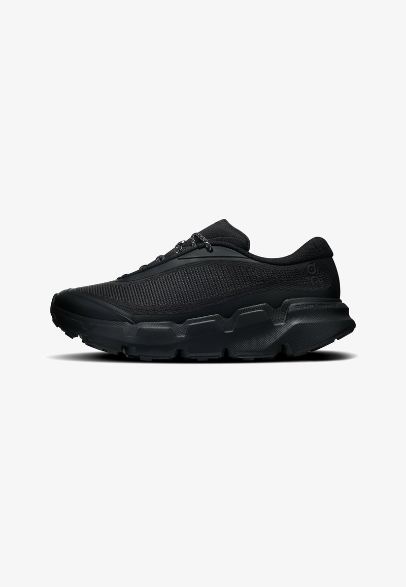 Chaussure de sport noire avec semelle épaisse texturée, dessus en mesh et lacets à motifs, vue de côté sur fond blanc.