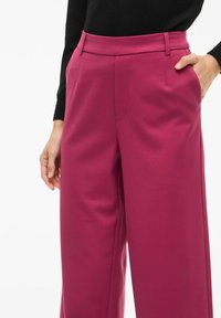 Pantalon large fuchsia à taille haute, poches latérales et texture lisse, complété par un haut noir élégant.