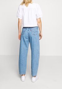 Světle modré denimové džíny s uvolněným střihem, vybavené středním pasem, standardními zadními kapsami a diskrétním štítkem značky na pase.