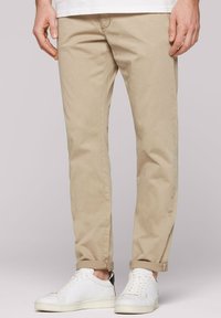 Beige chinos with a slim fit, featuring a smooth texture and rolled cuffs, paired with white sneakers with gray accents.