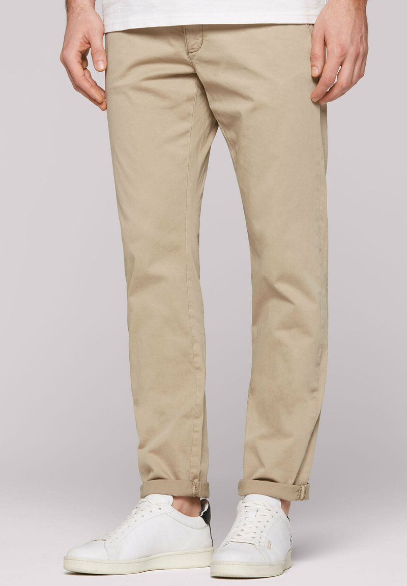 Beige chinos with a slim fit, featuring a smooth texture and rolled cuffs, paired with white sneakers with gray accents.