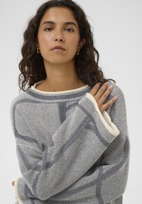 Pull en maille bleu marine et beige, avec une coupe ample, des manches larges et un motif texturé sur l'ensemble. Bordure crème au niveau de l'encolure.