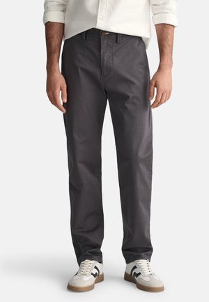Gray, straight-leg pants with a textured finish, featuring a front button closure, side pockets, and a relaxed fit, paired with white sneakers.