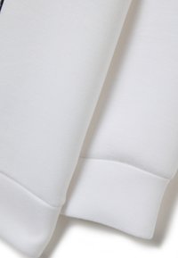 Sudadera blanca en primer plano, que muestra una tela suave, puños acanalados y una textura lisa. Presenta un diseño minimalista sin patrones.