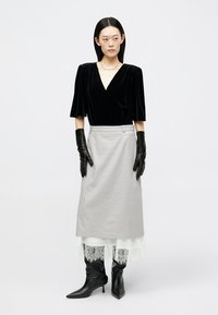 Musta samettitoppi, harmaa hame pitsireunuksella, mustat käsineet ja teräväkärkiset nilkkurit. Yksinkertaiset muodot ja tekstuurit luovat kerroksellisen ilmeen.