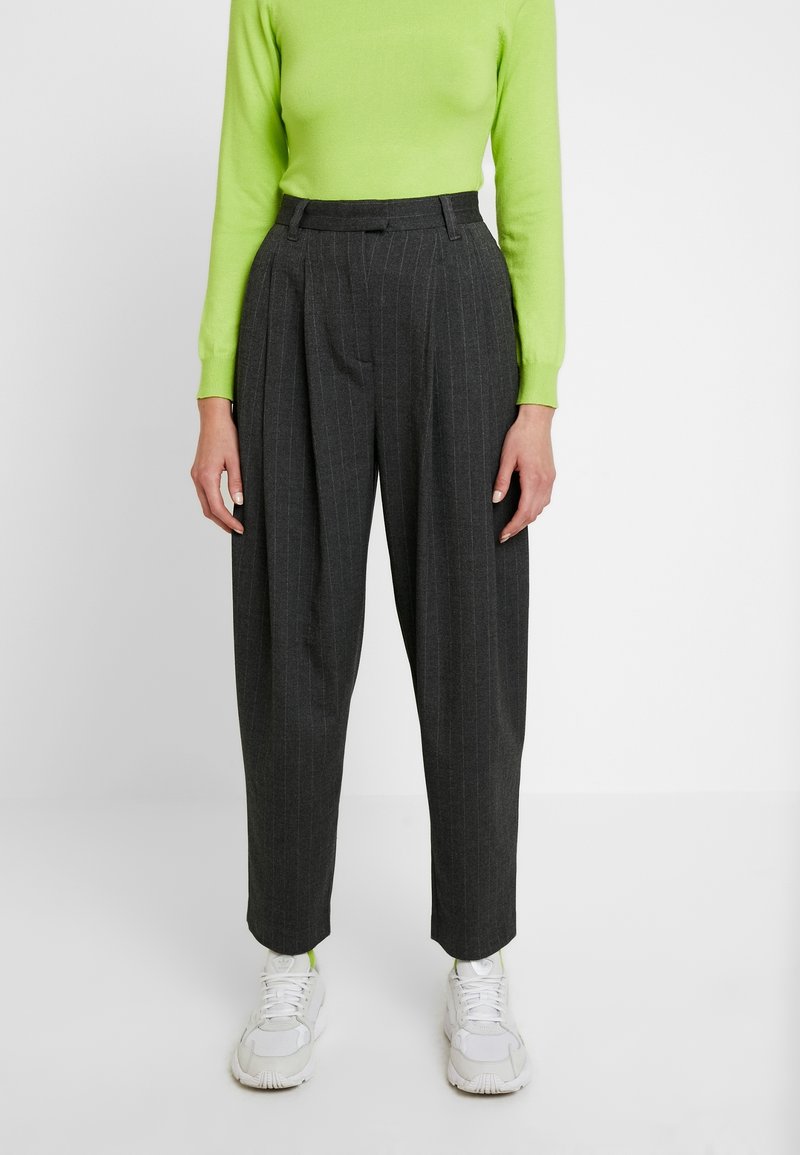 Pantalon gris à fines rayures avec taille haute, coupe ajustée et plis, associé à un haut à manches longues vert vif et des baskets blanches.