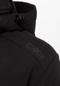 Musta vetoketjullinen takki, jossa on korkea kaulus ja teksturoitu kangas sekä pieni musta "CMP"-logo olkapäällä.