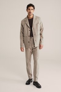 Helepruun villasest segumaterjalist ülikond, millel on bleiser takjakotiga ja sobivad püksid; kombineeritud mustade loafersidega. Sile tekstuur, viimistletud lõige.