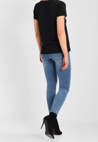 Camiseta negra de manga corta, jeans ajustados de color azul claro y botas de tacón alto negras hasta el tobillo. Tejido suave, diseño ajustado, detalles mínimos.