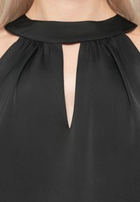 Detalhe de um top halter preto com decote em forma de olho-chave, mostrando pele na parte central da frente.