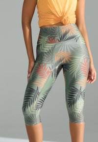 Leggings Capri con base verde e motivo a foglie multicolore nelle tonalità di arancione, nero e verde. Design elastico e aderente.