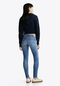 Sudadera corta de punto de cable en color navy con capucha, combinada con jeans skinny azul claro y zapatillas beige con suela de goma.