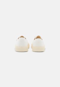 Baskets en toile blanche avec un bout arrondi, une semelle en caoutchouc beige texturée et une couture contrastée à l'arrière. Design simple et minimaliste.